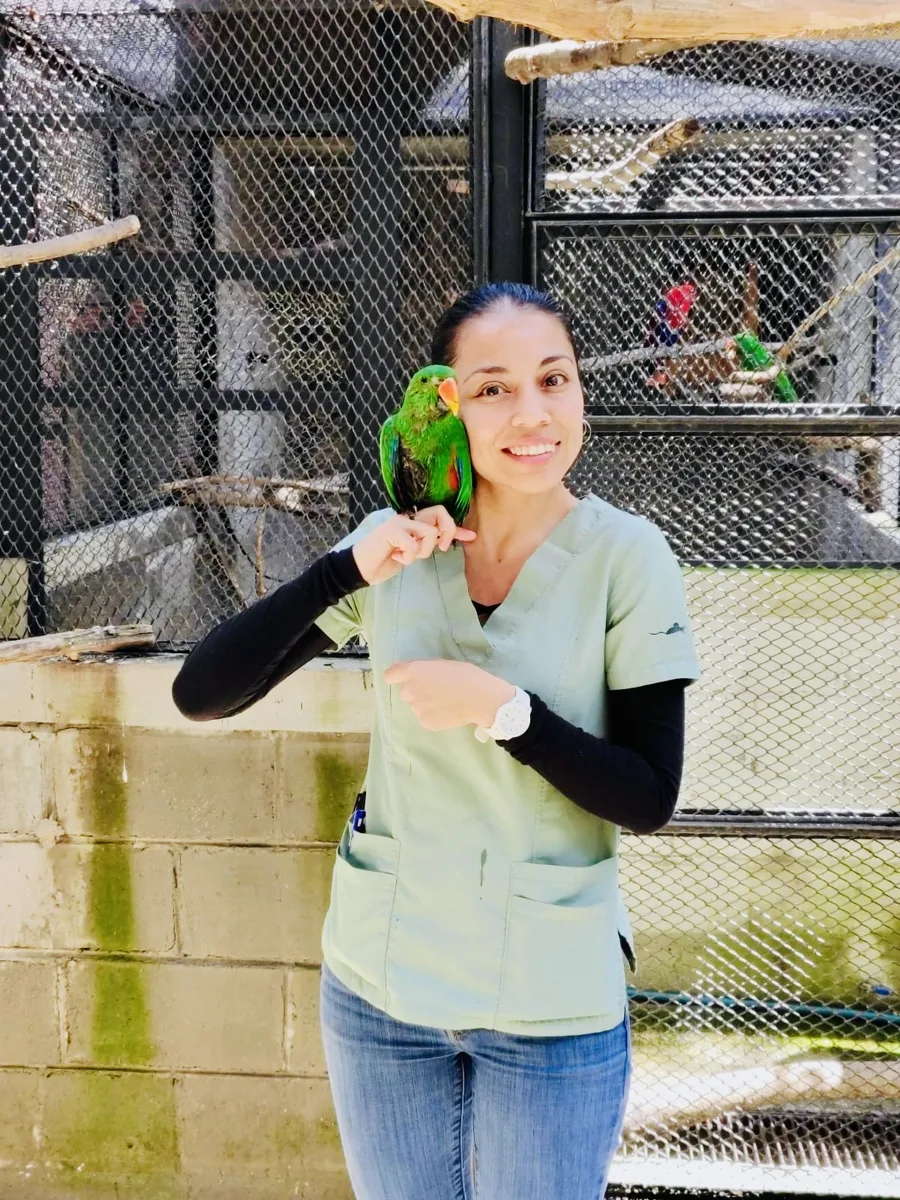 La Dra. Carolina Flores con un loro verde posado en su hombro, en el aviario
